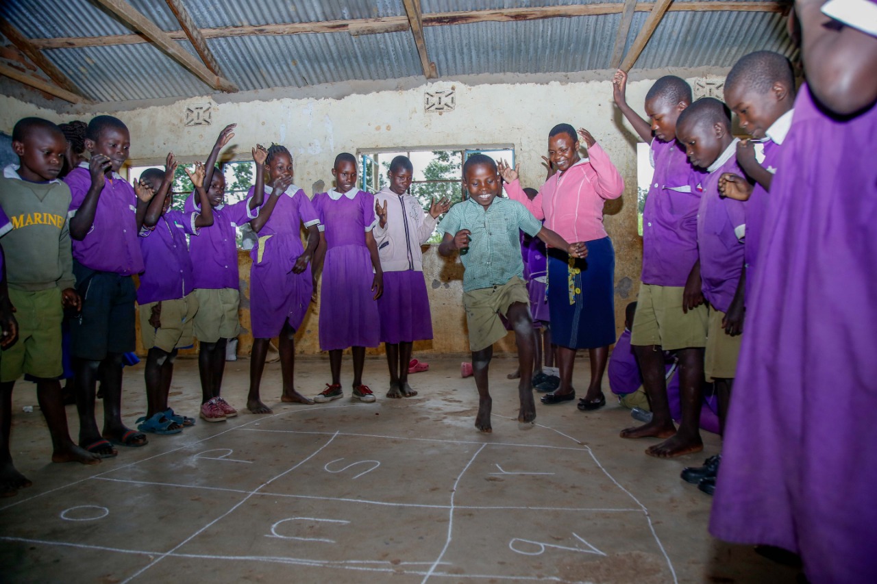 Children playing a hopscotch-style learning game with their teacher
